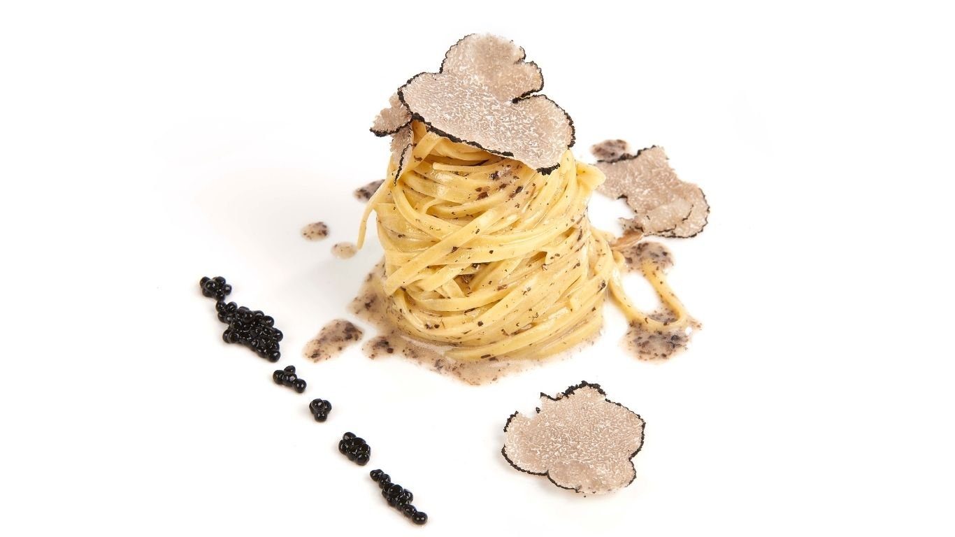 Чиния спагети, гарнирани с черен трюфел, поднесени с черен хайвер отстрани.